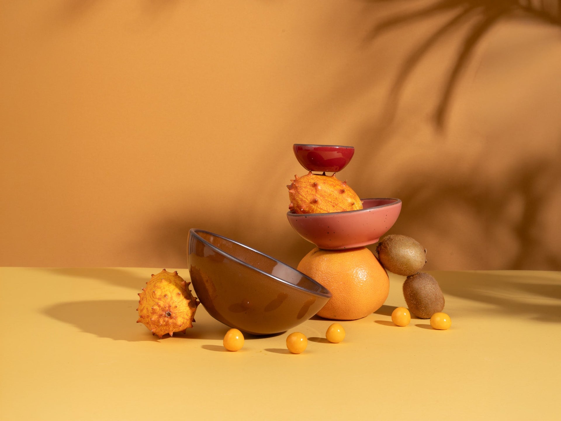Ceramic bowls in various colors artfully arranged with fruit on a golden background.