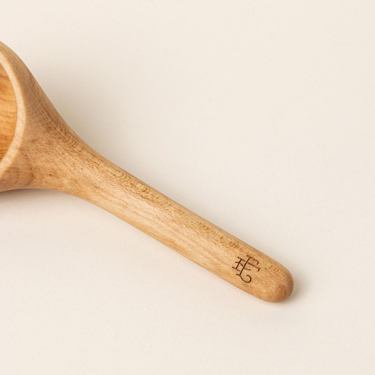 A close up of the end of a handle of a short wooden coffee scoop with an East Fork logo stamp