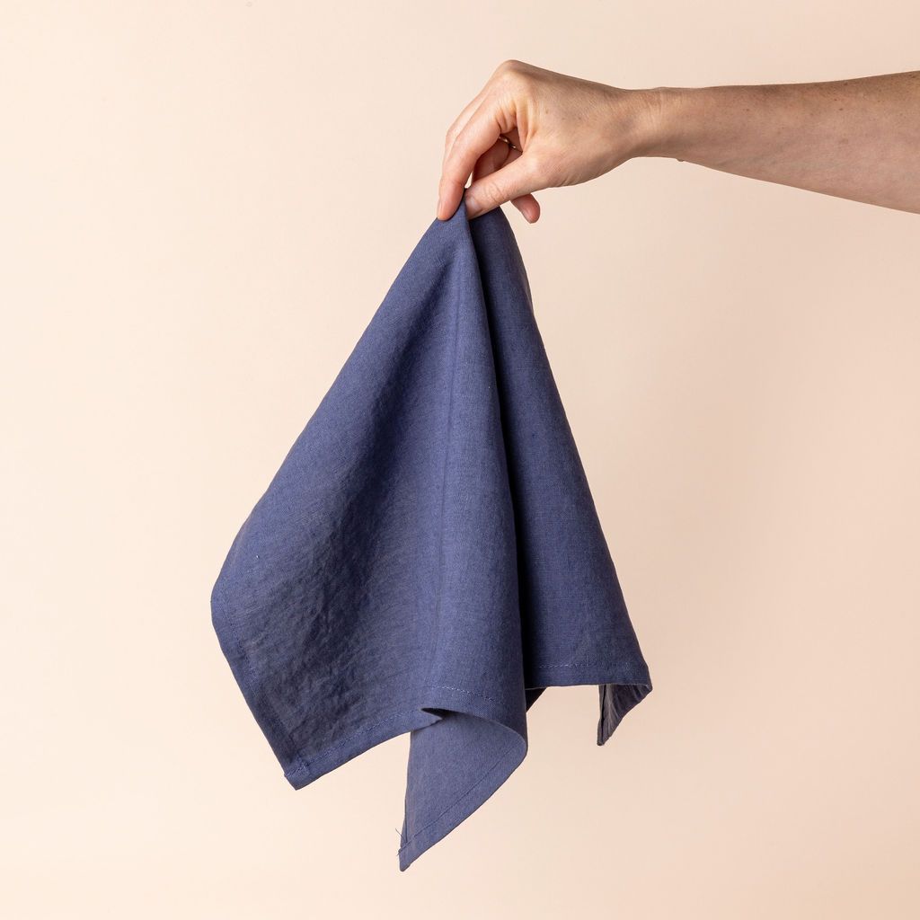Hand holding a linen napkin in a muted blue color from the center