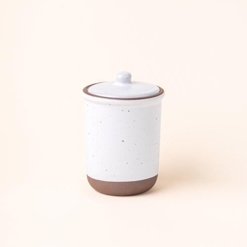 A tall ceramic lidded jar in a cool white color with an unglazed base.