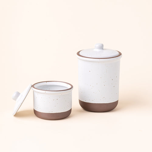 A small and tall ceramic lidded jars in a cool white color with an unglazed base.