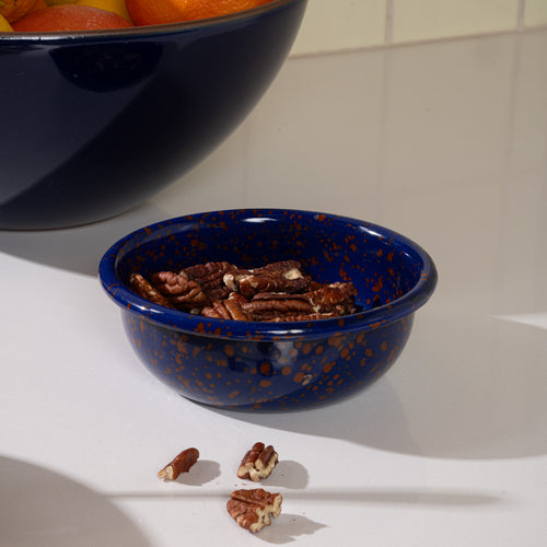 A small enamel bowl in midnight blue color with red splatter pattern, filled with pecans.