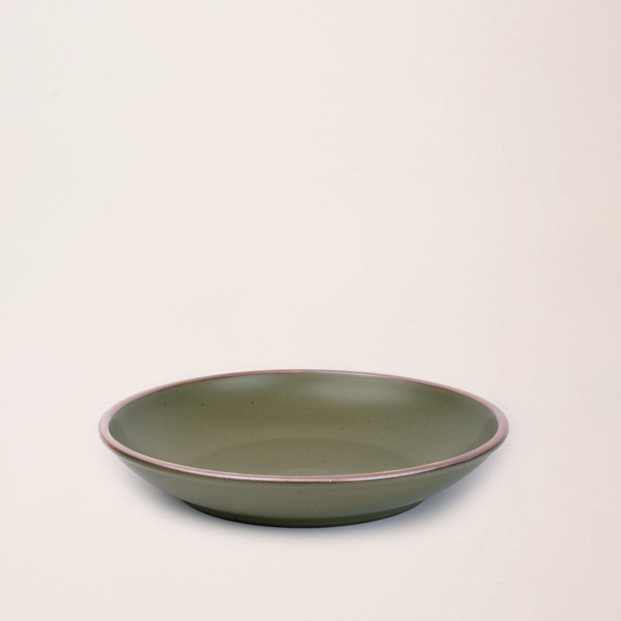 A medium side ceramic plate with a curved bowl edge in an olive green color featuring iron speckles and an unglazed rim.