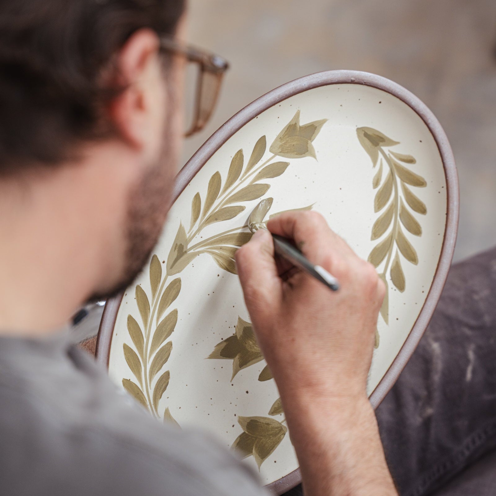 Alex painting decorative greenery on a medium ceramic oval platter.