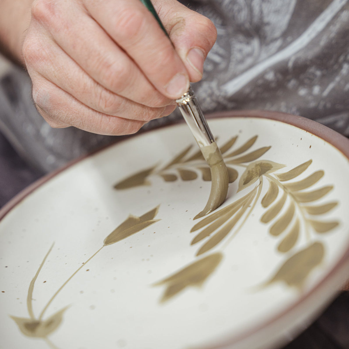 Closeup of Alex painting decorative greenery on a medium ceramic oval platter.