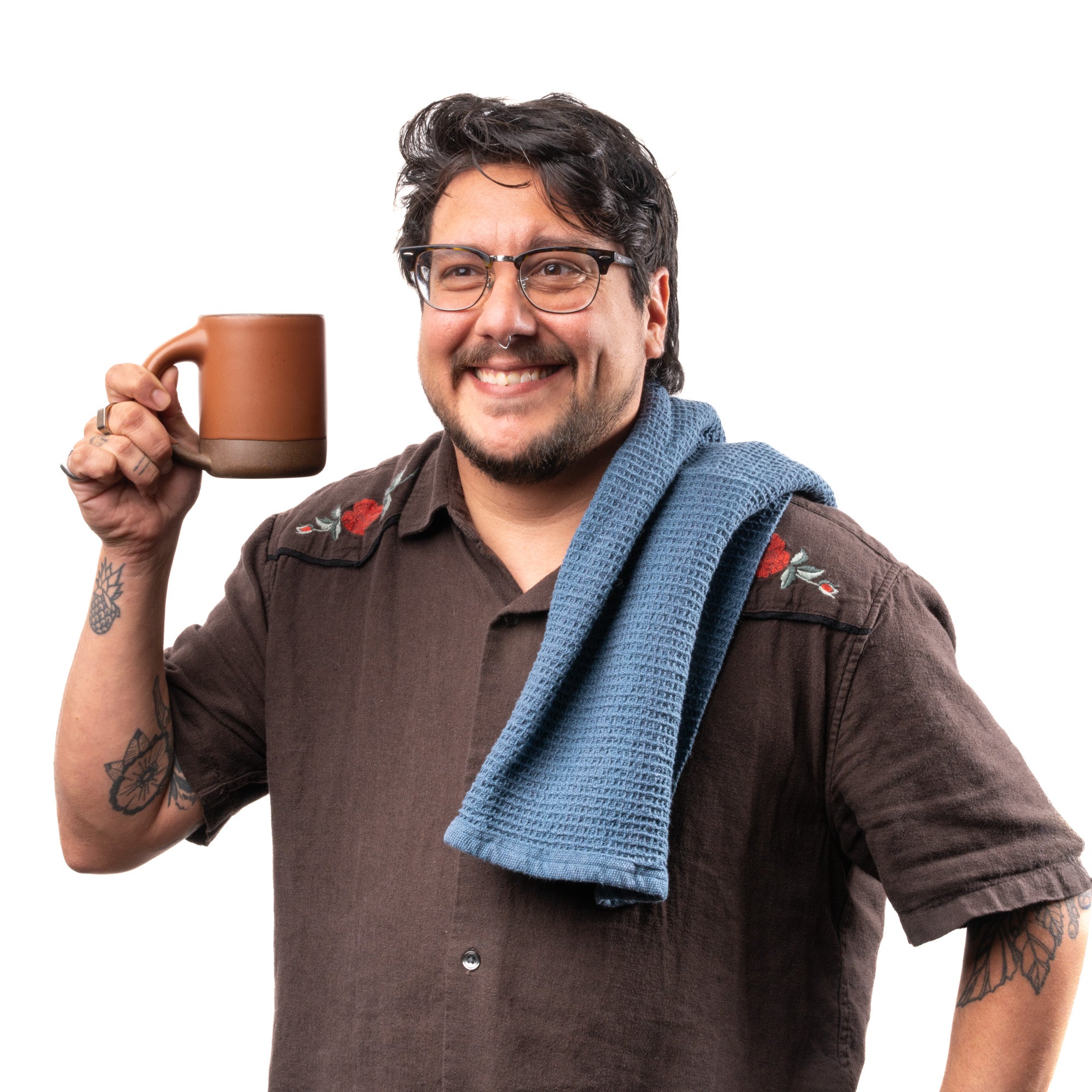 Elliot smiling holding an East Fork mug and a blue kitchen towel resting on their shoulder.