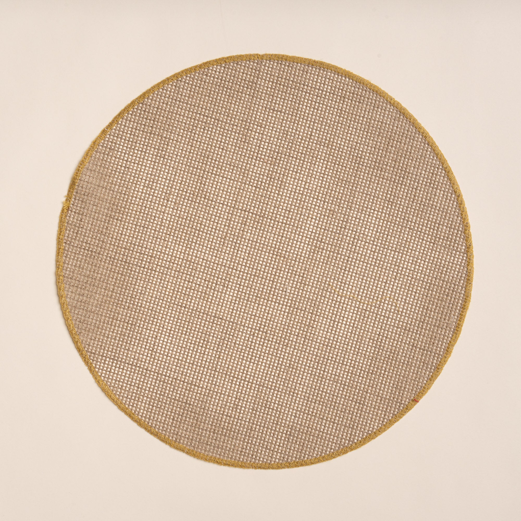 Round woven placemat in a natural color with a sewn ochre rim on a beige background