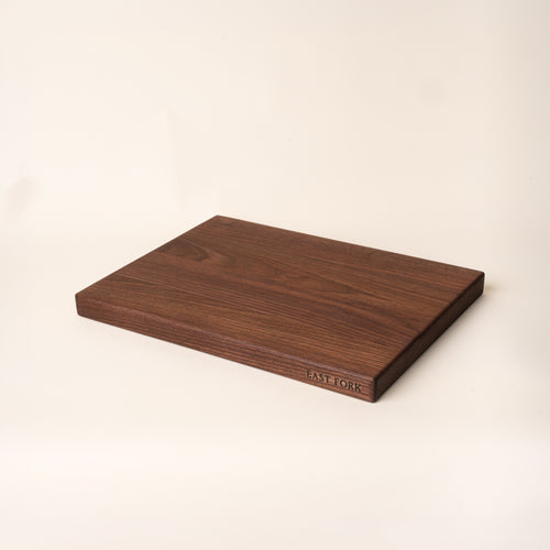 A medium rectangular walnut cutting board on its side with an engraving on the edge that reads 'East Fork'