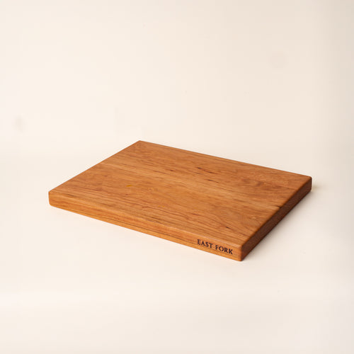 A medium rectangular cherry cutting board on its side with an engraving on the edge that reads 'East Fork'