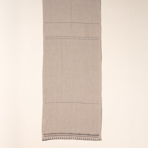 A neutral table runner, partially folded to showcase contrasting hand-stitched details in navy and rust.