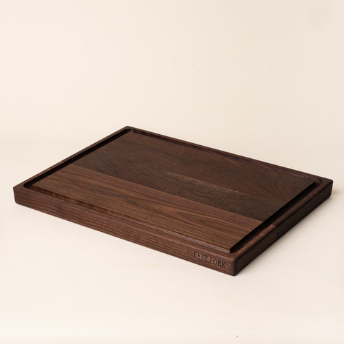 A large rectangular walnut cutting board on its side with a juice groove and an engraving on the edge that reads 'East Fork'