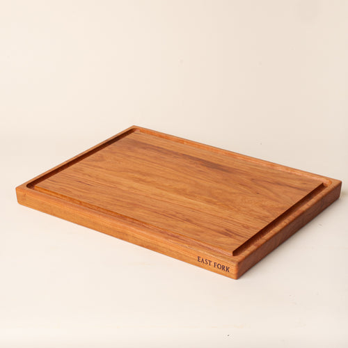A large rectangular cherry cutting board on its side with a juice groove and an engraving on the edge that reads 'East Fork'