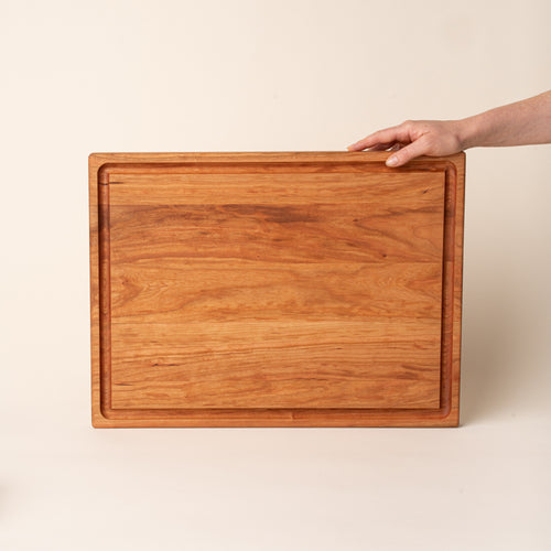 A hand props up a large rectangular cherry cutting board on its side with a juice groove