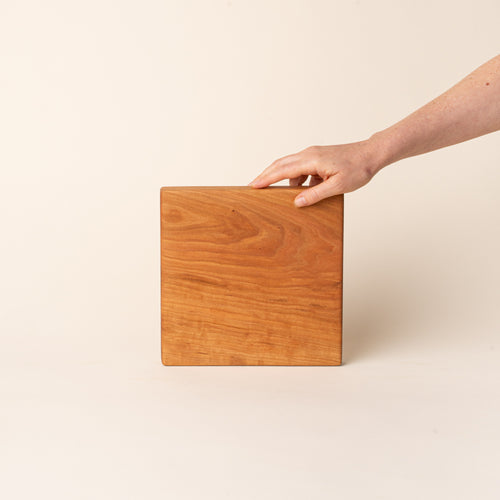 A hand props up a square cherry cutting board on its side