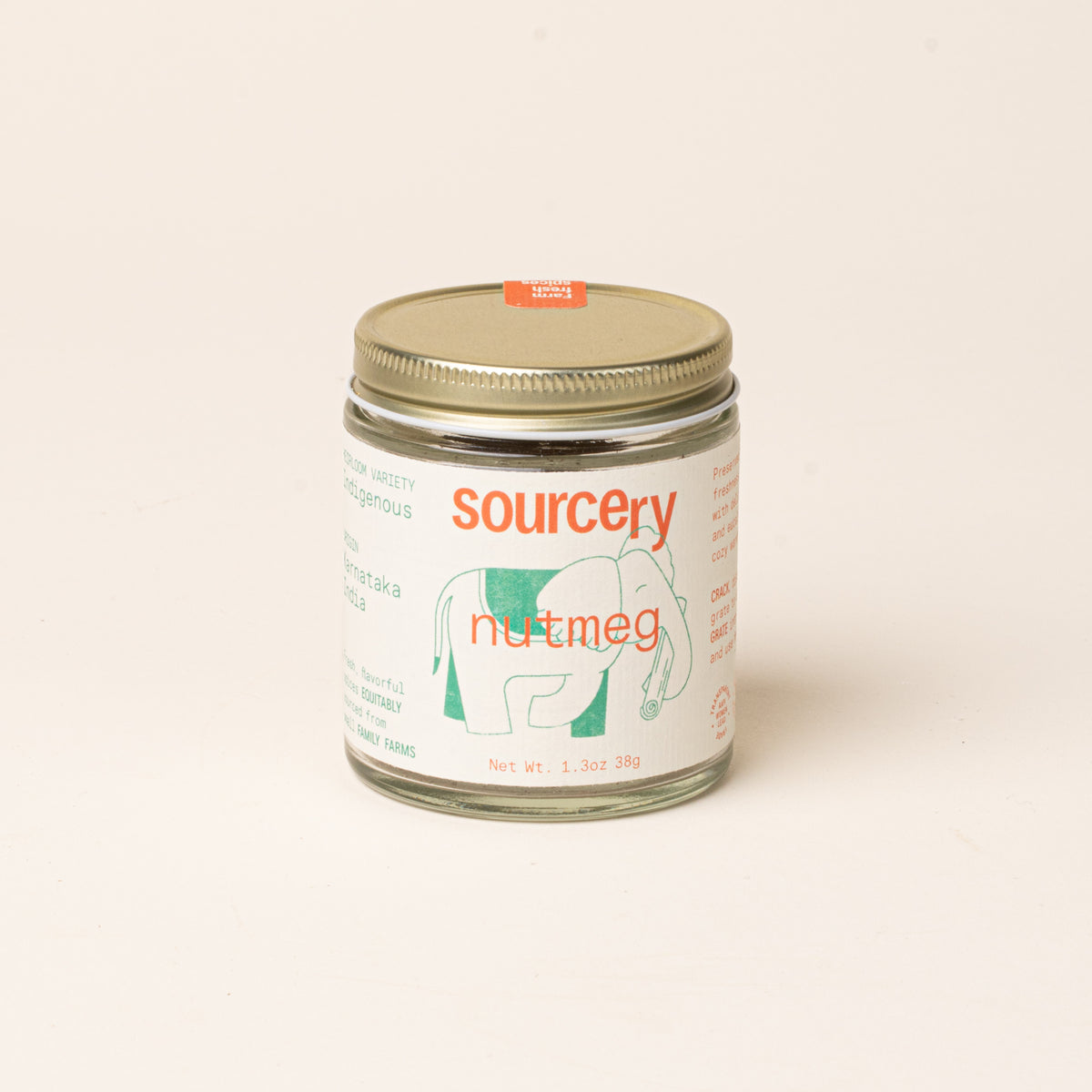 Glass jar of Sourcery nutmeg with a gold metal lid and a cream label featuring orange lettering and a green elephant illustration.