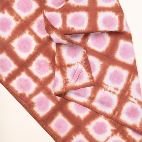 A closeup of a tie-dye tea towel in a pink colorway with a hanging corner tag