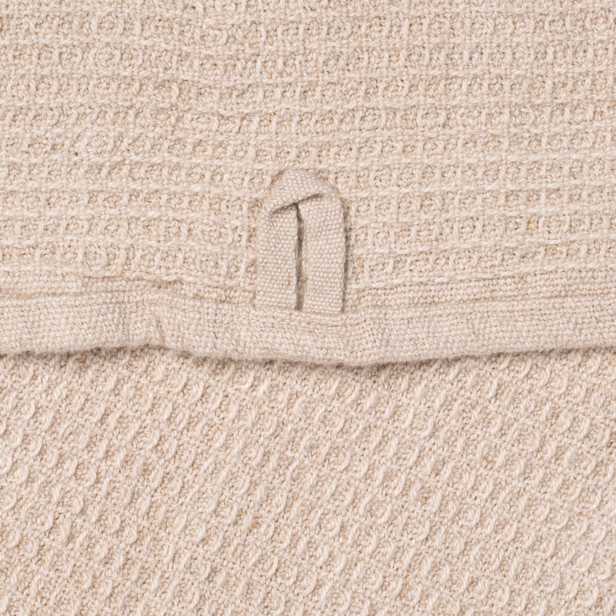 A closeup of a natural waffle weave kitchen towel, with a hanging loop.