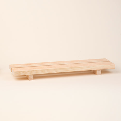 A long, low unfinished-wood bath tray made from two parallel planks, with simple block feet. 
