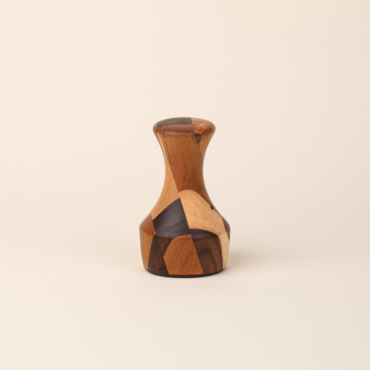 Sculptural wooden biscuit cutter with a tapered neck, flared top, and geometric patchwork of light and dark wood tones.
