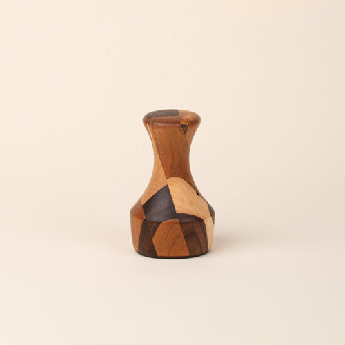 Sculptural wooden biscuit cutter with a tapered neck, flared top, and geometric patchwork of light and dark wood tones.