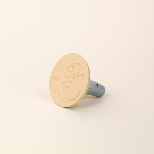 Hand holding a cookie stamp showing the bottom featuring the design of a lily of the valley