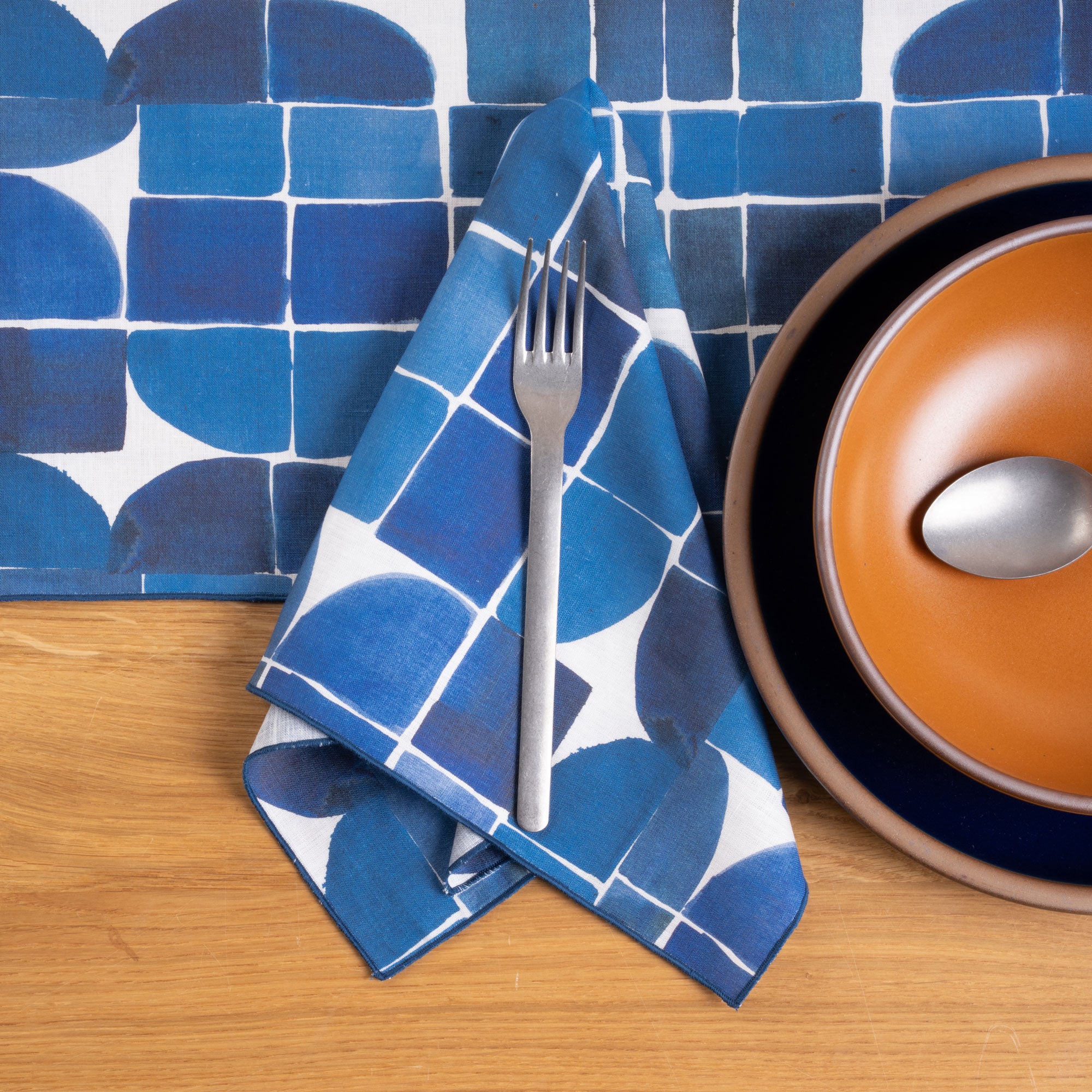 Blue geometric napkin and tablecloth paired with warm orange and deep navy dinnerware on a wood table.