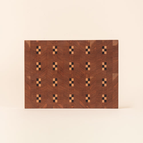Rectangular wooden cutting board with repeating geometric inlay pattern on a light background.