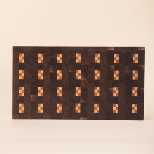 Dark rectangular wooden cutting board with repeating light geometric inlay pattern on a white background.