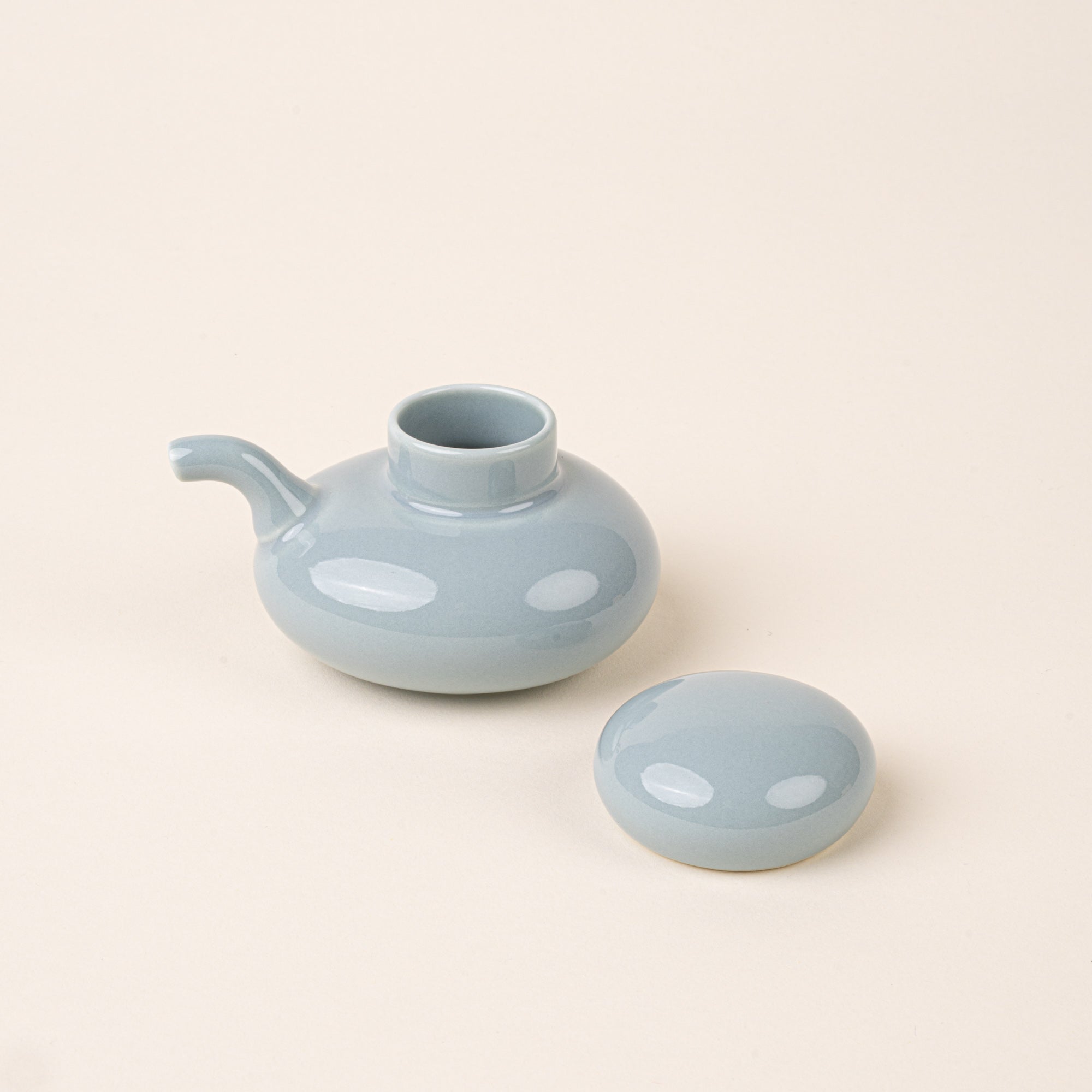 A pale blue glazed ceramic soy sauce pot with a low, rounded body, short pouring spout, and domed lid to the side.