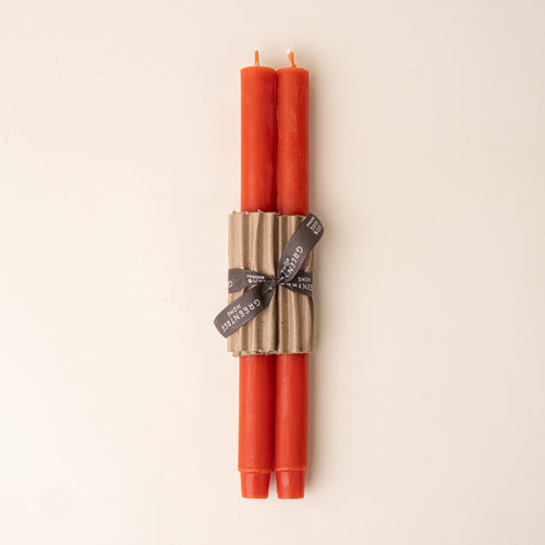 Two orange taper candles bundled with corrugated cardboard and tied with a black ribbon on a neutral background.