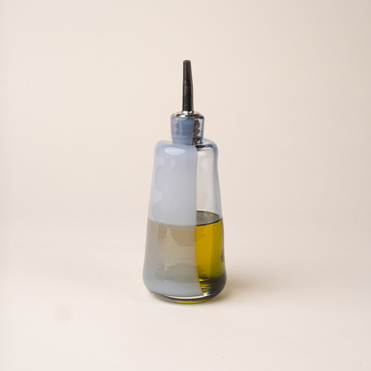 A blue-gray glass oil or vinegar dispenser with a polished metal pour spout and stopper, filled with oil.