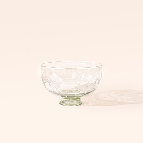 A smaller clear glass footed bowl with etched floral designs, on a cream background.