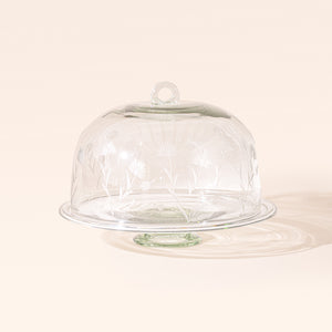 An etched floral glass dome on a clear glass cake stand.