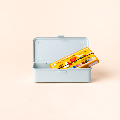 Open light blue rectangular storage box holding a yellow and orange box of crayons, with the hinged lid upright against a cream background.