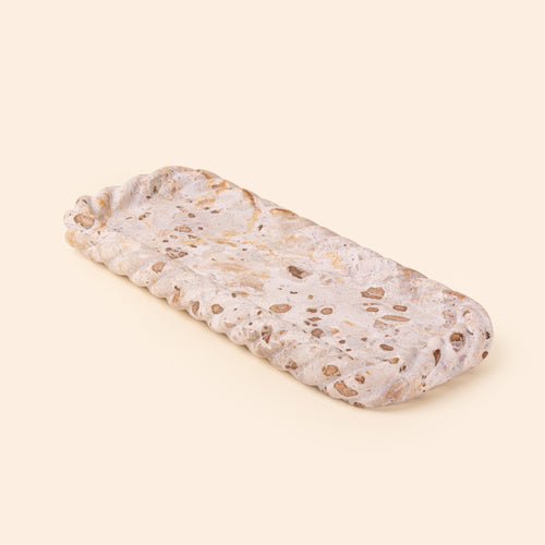 Rectangular cream and brown speckled stone tray with a shallow recessed center and irregular scalloped edges.