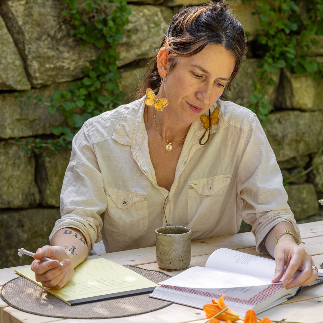 Connie sitting at a table outside reading Taste of Country Cooking and writing on a yellow notepad