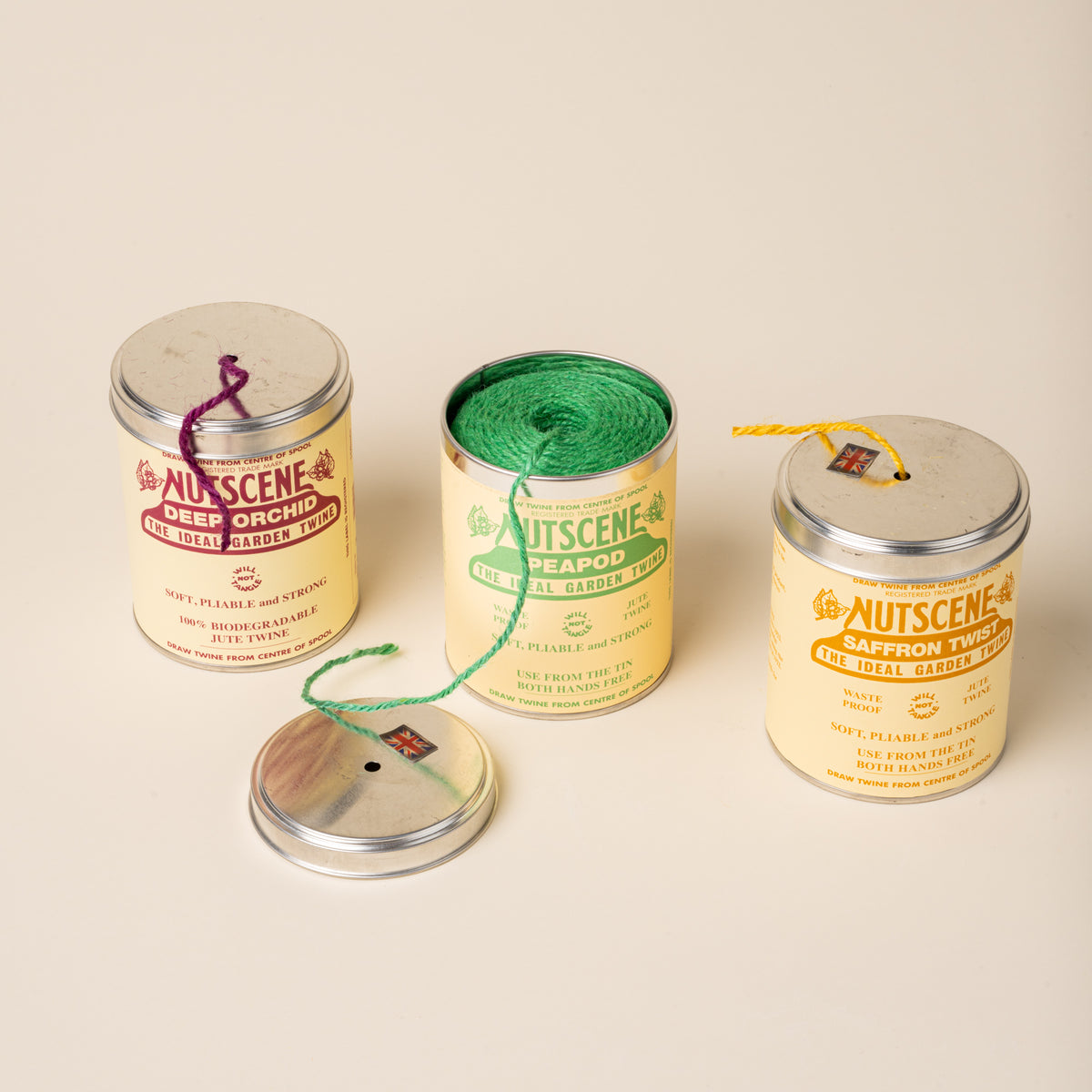 Three Nutscene garden twine tins, one open showing green twine, with loose lids and colored strands visible.