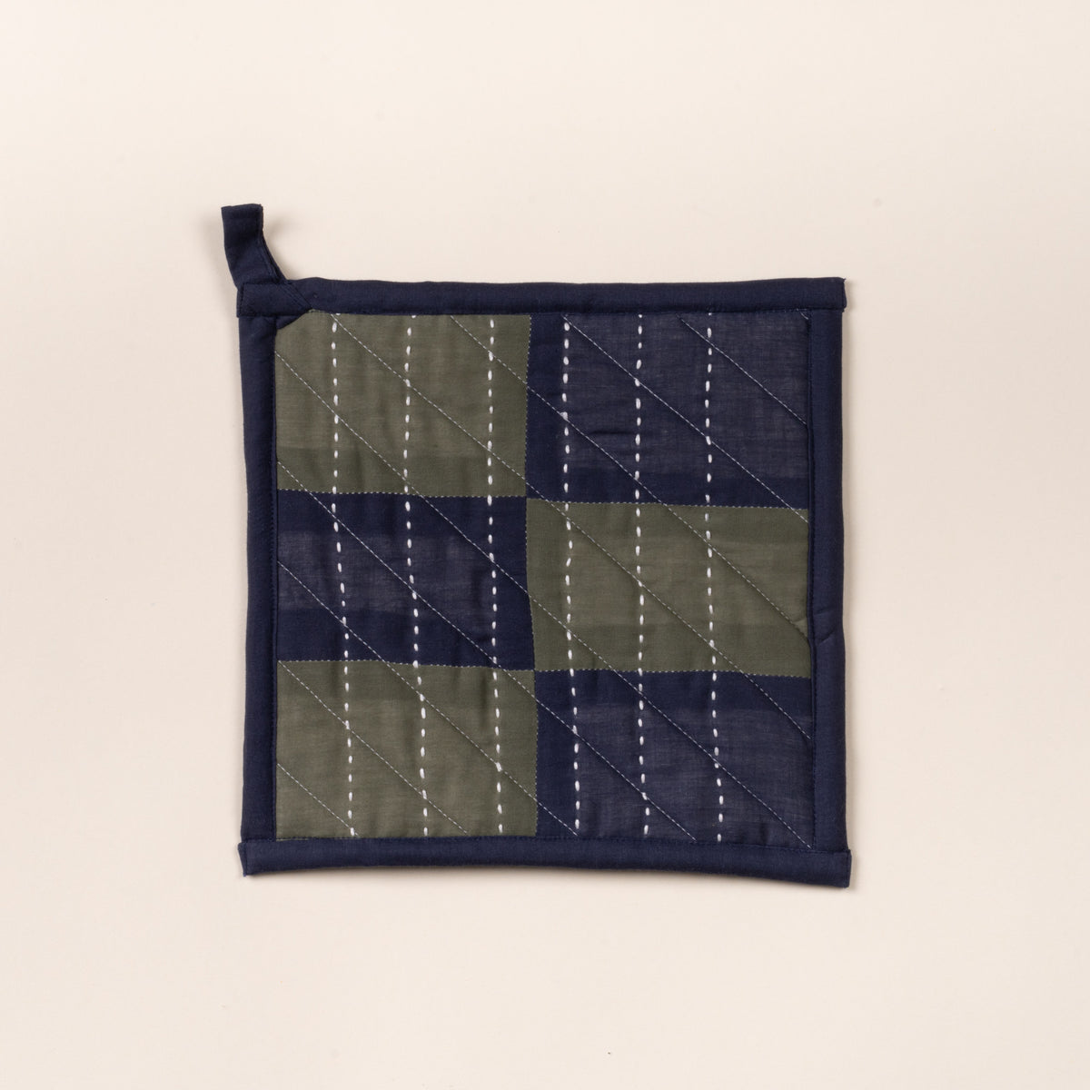 Quilted pot holder with green and navy patchwork squares and white stitched lines, with hanging loop.