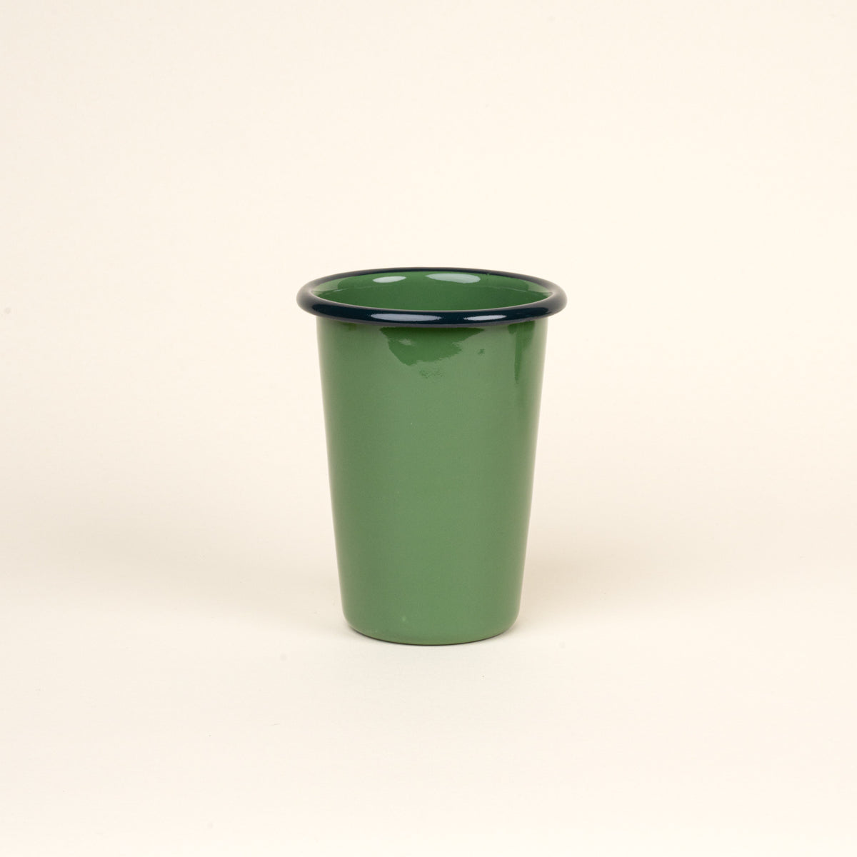 A tall green enamel tumbler with a dark rim, set against a soft beige background.