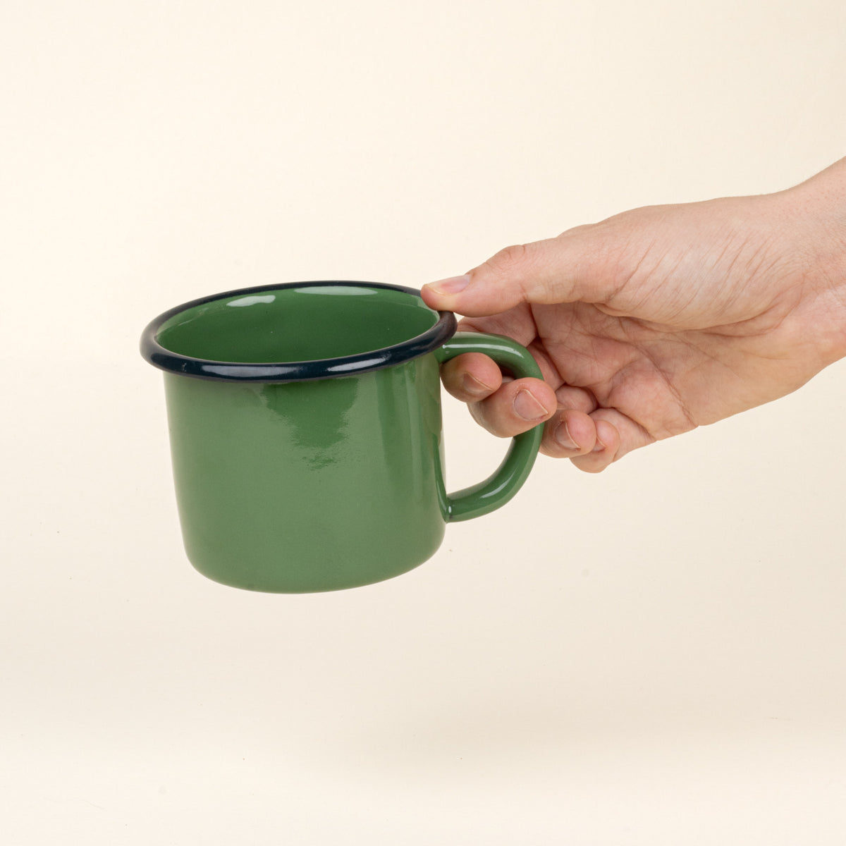 Hand holds a green enamel mug with a dark rim and handle