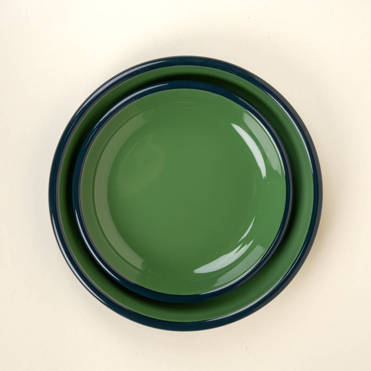 A nesting enamel side plate and dinner plate in green with a dark rim.
