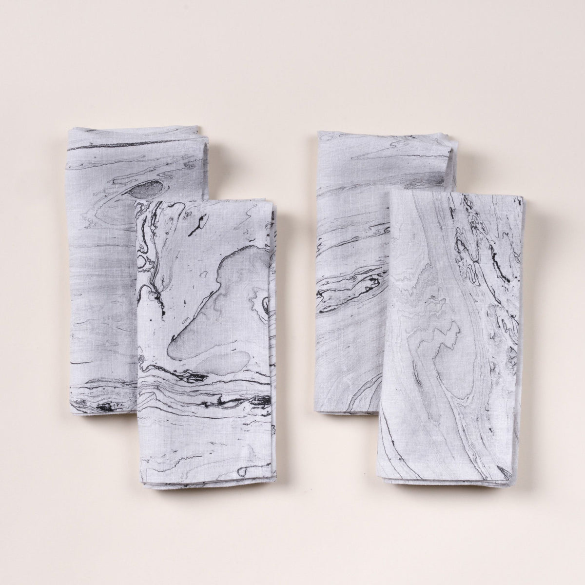 Four folded napkins with a gray marble-like pattern arranged on a light background.