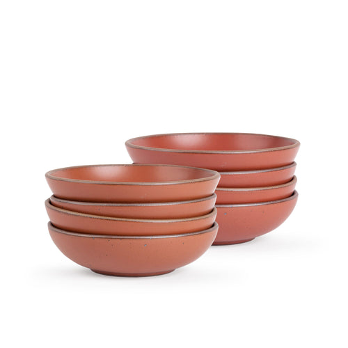 A stack of 8 dinner-sized shallow ceramic bowls in a cool burnt terracotta color featuring iron speckles and an unglazed rim