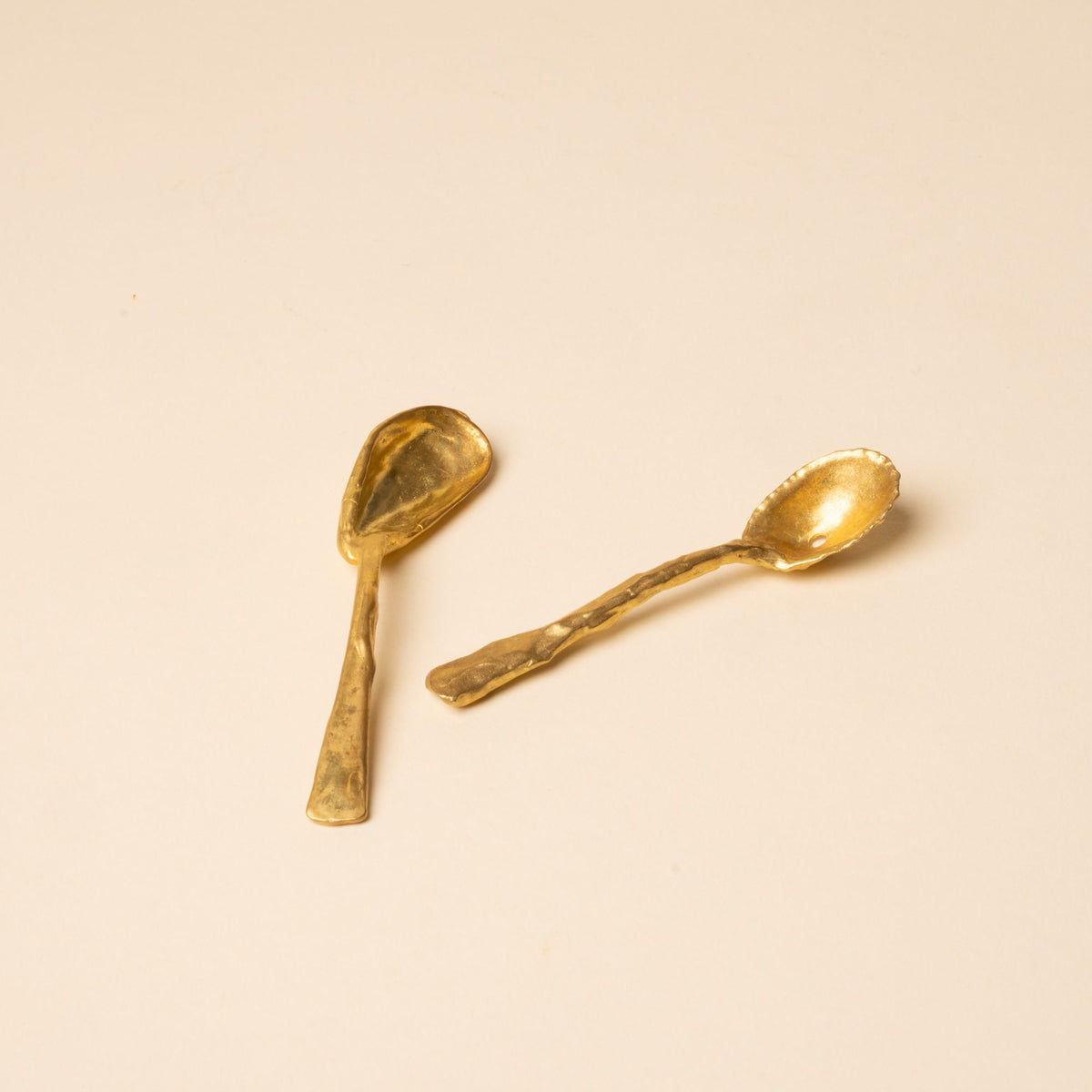 Two small handcrafted gold spoons with textured, organic shapes on a neutral background.