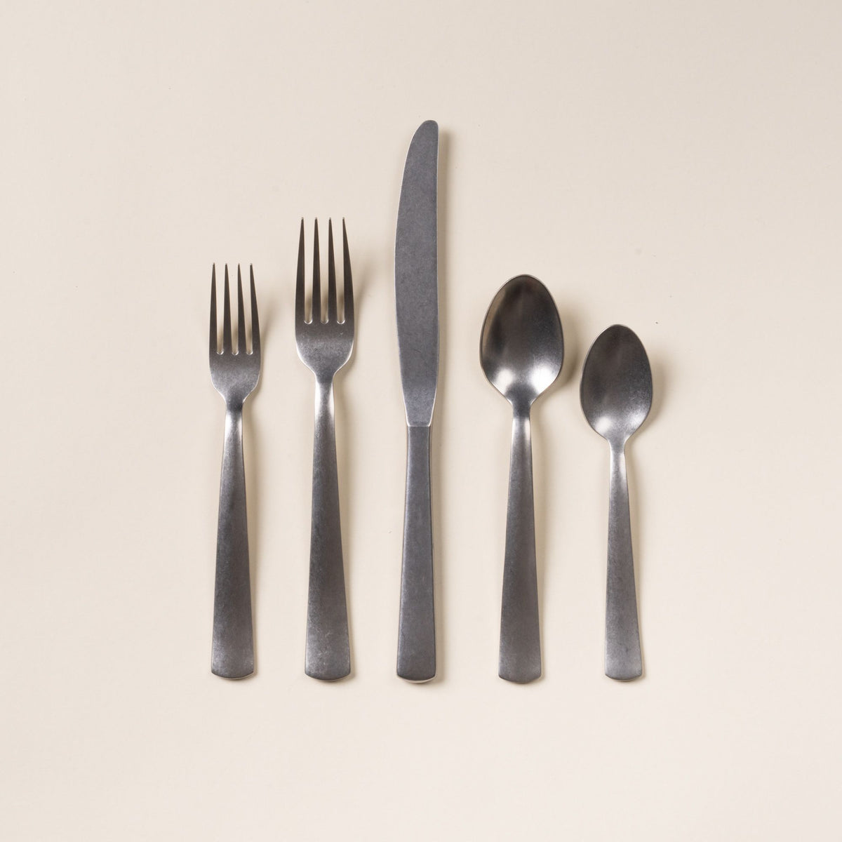 Five matte stainless steel utensils—salad fork, dinner fork, knife, tablespoon, and teaspoon—arranged on a neutral background.