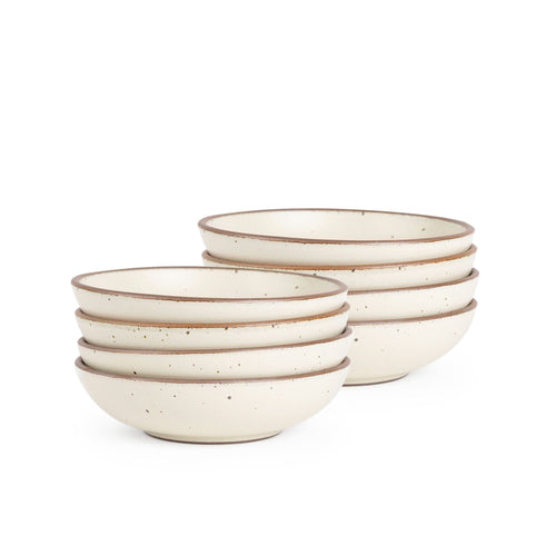A stack of 8 dinner-sized shallow ceramic bowls in a warm off-white color featuring iron speckles and an unglazed rim
