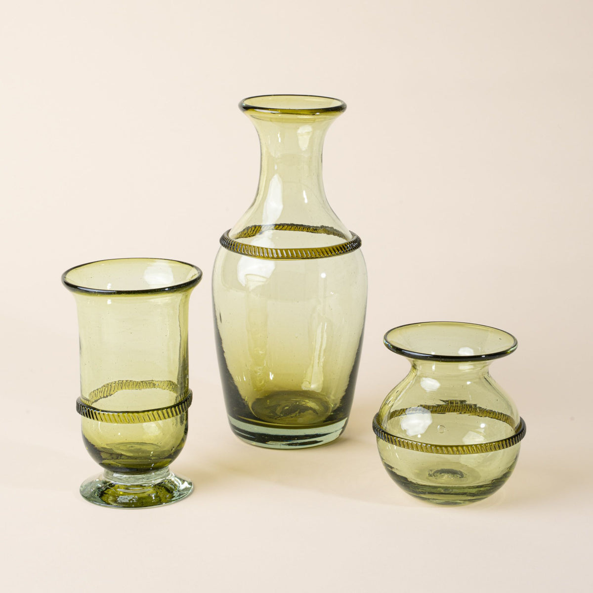 Set of three light green glass vessels—a tall flared vase, a pedestal vase, and a small rounded vase—each with a decorative band around the center, displayed against a neutral background.