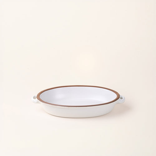 A medium, oval, matte, cool white ceramic baking dish with two side handles, on a solid off-white background.