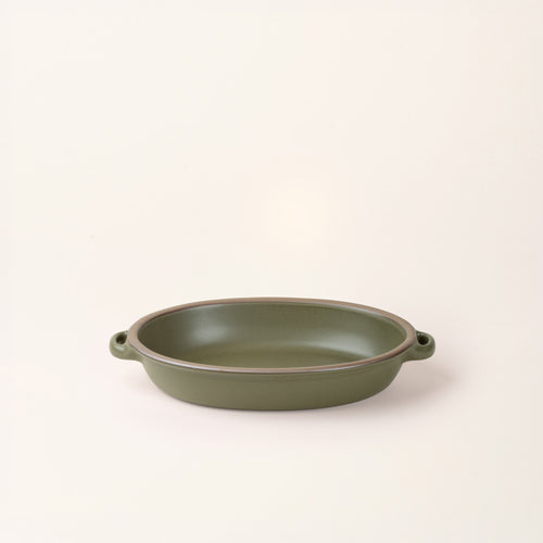 A medium oval, matte olive green ceramic baking dish with two side handles, on a clean, solid off-white background.