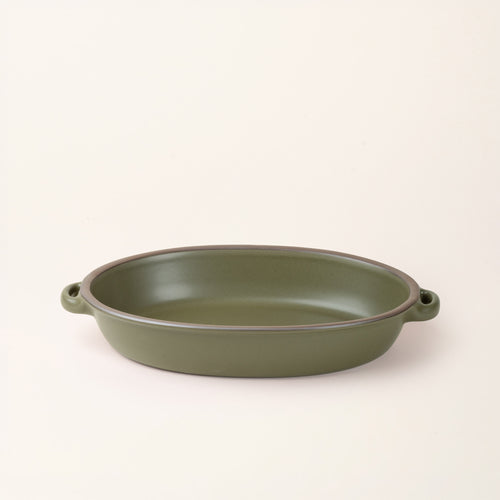 A large, oval, matte, olive green ceramic baking dish with two side handles, on a solid off-white background.